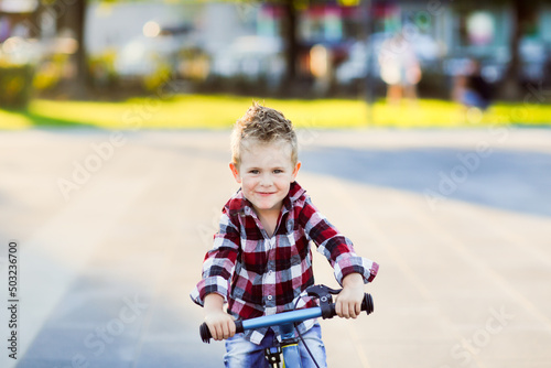 stylish European boy in shirt and jeans rides balance bike on asphalt. Child riding without helmet