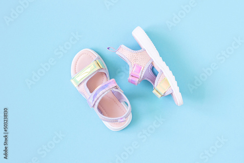 Stylish holographic sandals for kids on blue background. Shiny fashion summer shoes. Flat lay, Top view