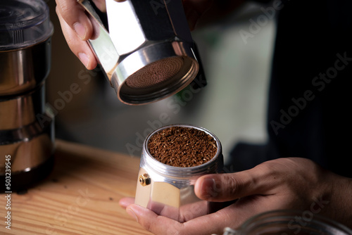 Barista holding moka pot with ground coffee in coffee shop. photo