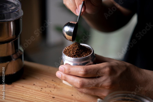 Barista holding moka pot with ground coffee in coffee shop.
