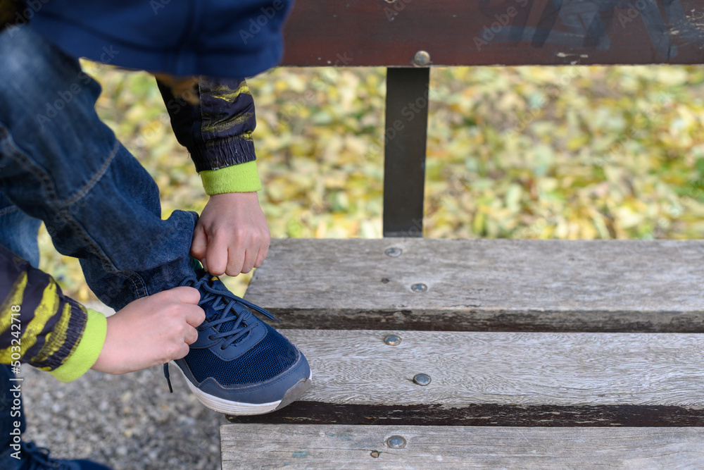 Child laces up a sneaker on a park bench Child laces up a sneaker on a park bench
