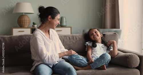 Affectionate excited Indian mommy tickle happy laughing preschool age daughter on comfy sofa enjoy weekend at cozy home together with child. Active mom nanny little girl relax play funny game have fun