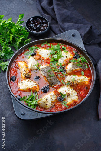 Traditional Spanish seafood zarzuela de pescado with fish served in red sauce as top view in design pot