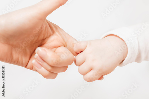 ukrainian baby holds mom's index finger on a white background. close up. emotional connection between mother and child. The grasping reflex in a child. Family, love, friendship.