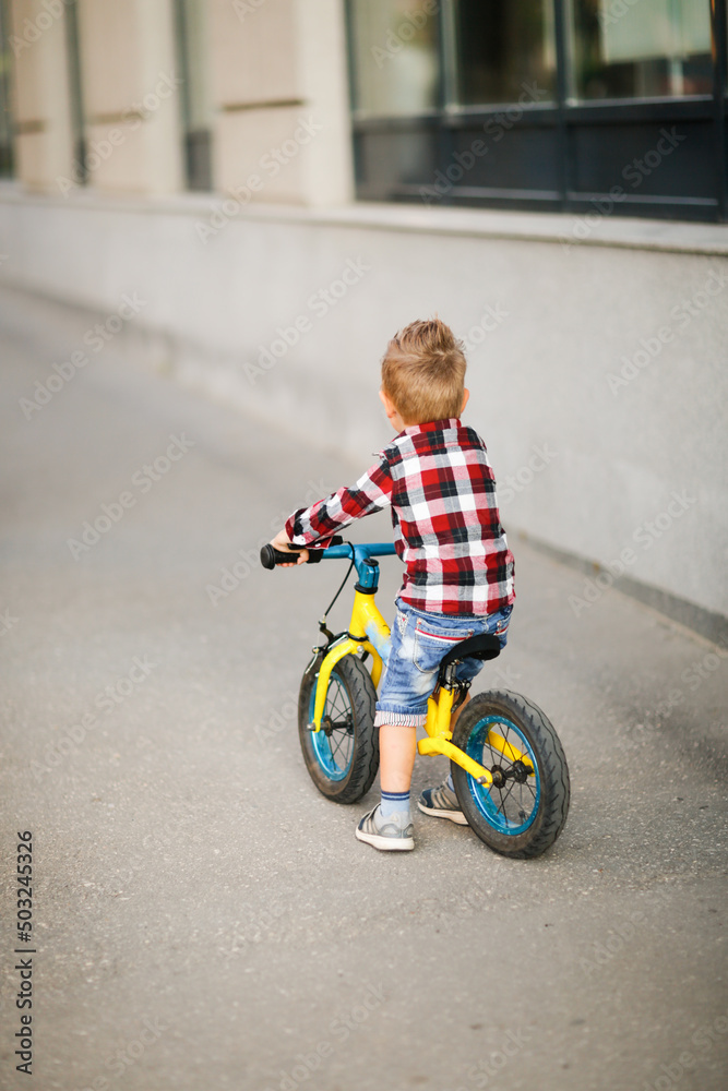 Stylish boy ride on balance bike on sidewalk in city Stylish boy ride on balance bike on sidewalk in city