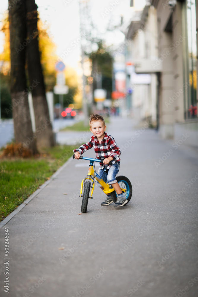 Stylish boy ride on balance bike on sidewalk in city