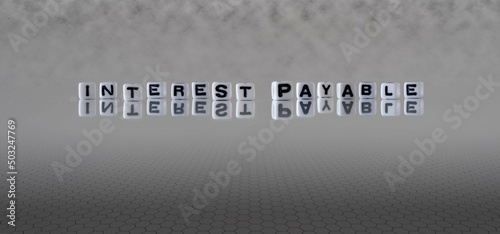 interest payable word or concept represented by black and white letter cubes on a grey horizon background stretching to infinity