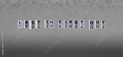 last in first out word or concept represented by black and white letter cubes on a grey horizon background stretching to infinity