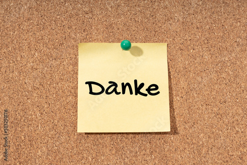 Thanks word in german language on yellow note on cork board