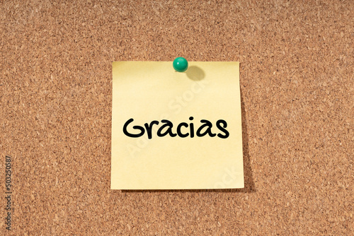 Thanks word in spanish language on yellow note on cork board