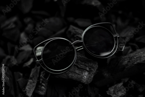 Glasses, black lenses, round shape, on a charcoal black background, are cool