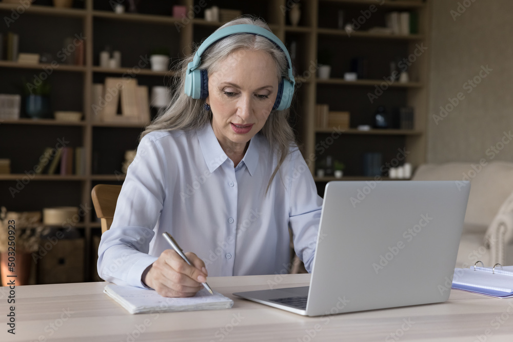 Focused older student in wireless headphones watching virtual workshop ...