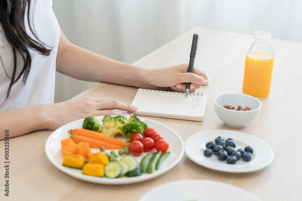 Diet, Dieting hand of woman write diet plan right nutrition on table with fresh vegetables salad, almond is different food ingredients in the green. Nutritionist of healthy, nutrition of weight loss. Diet, Dieting hand of woman write diet plan right nutrition on table with fresh vegetables salad, almond is different food ingredients in the green. Nutritionist of healthy, nutrition of weight loss.