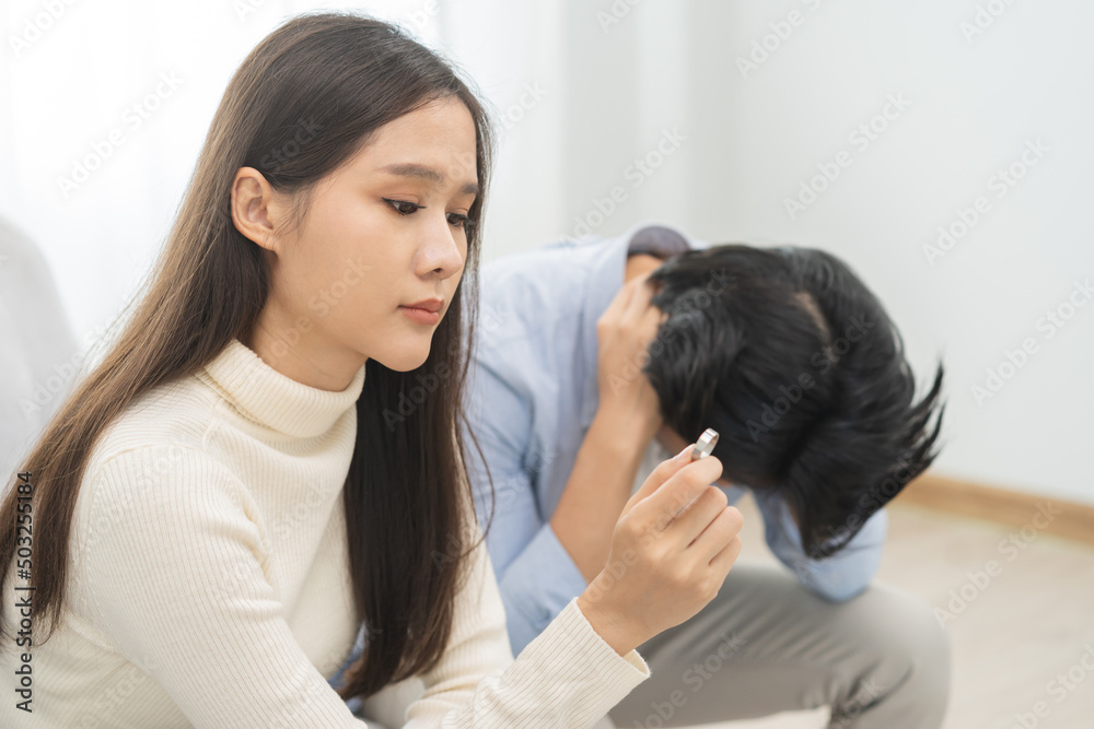 Stressed asian young couple man, woman quarrel on couch, relationship in trouble. Wife's hand holding wedding ring in disappointment and upset her husband, which may lead to divorce. Problem of family Stressed asian young couple man, woman quarrel on couch, relationship in trouble. Wife's hand holding wedding ring in disappointment and upset her husband, which may lead to divorce. Problem of family