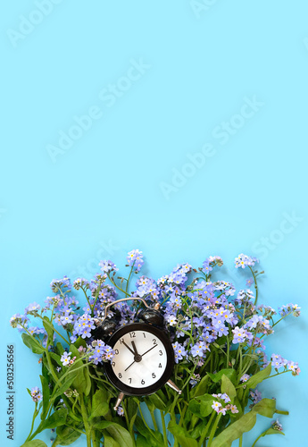 Clock alarm and blue flowers forget me not on abstract blue  background. spring seasonal composition. spring time symbol. top view. copy space
