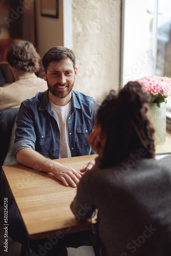 Handsome happy man smiling and sitting at table in cafe with friend. Caucasian male at date concept.