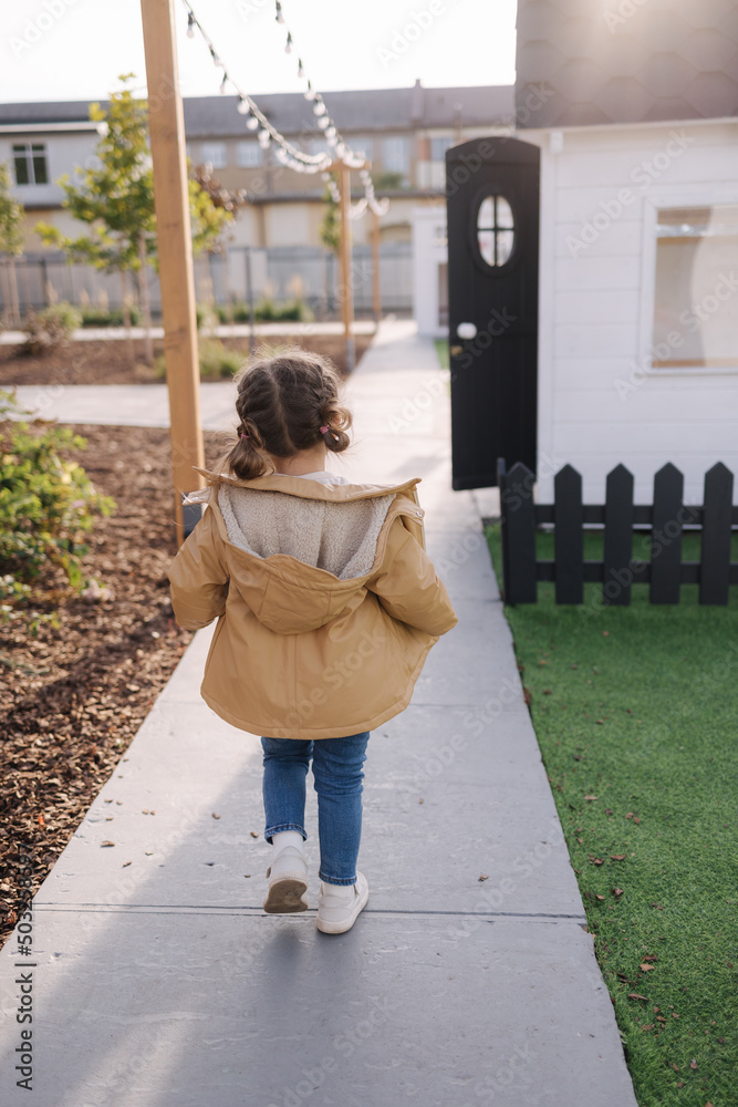 Back view of little girl walking in little kids city. Toy city for children outdoors. Road for walking Back view of little girl walking in little kids city. Toy city for children outdoors. Road for walking