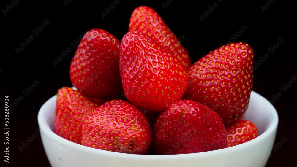 Strawberries without tails lie in white bowl or plate. It rotates on its axis on black background. Strawberry dessert. Appetizing summer berries in combination with black color. Vitamins and luxury. Strawberries without tails lie in white bowl or plate. It rotates on its axis on black background. Strawberry dessert. Appetizing summer berries in combination with black color. Vitamins and luxury.