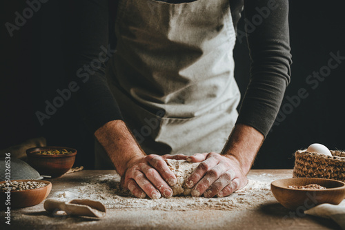 Canvastavla Young man kneading dough on dark background.