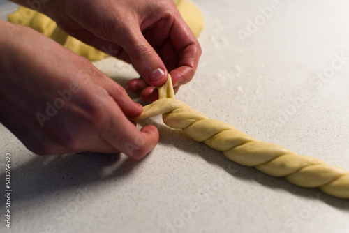 Female hands braiding dough on white kitchen table, close up