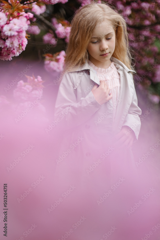 Portrait of a gorgeous little girl in the background of a blooming Japanese sakura tree