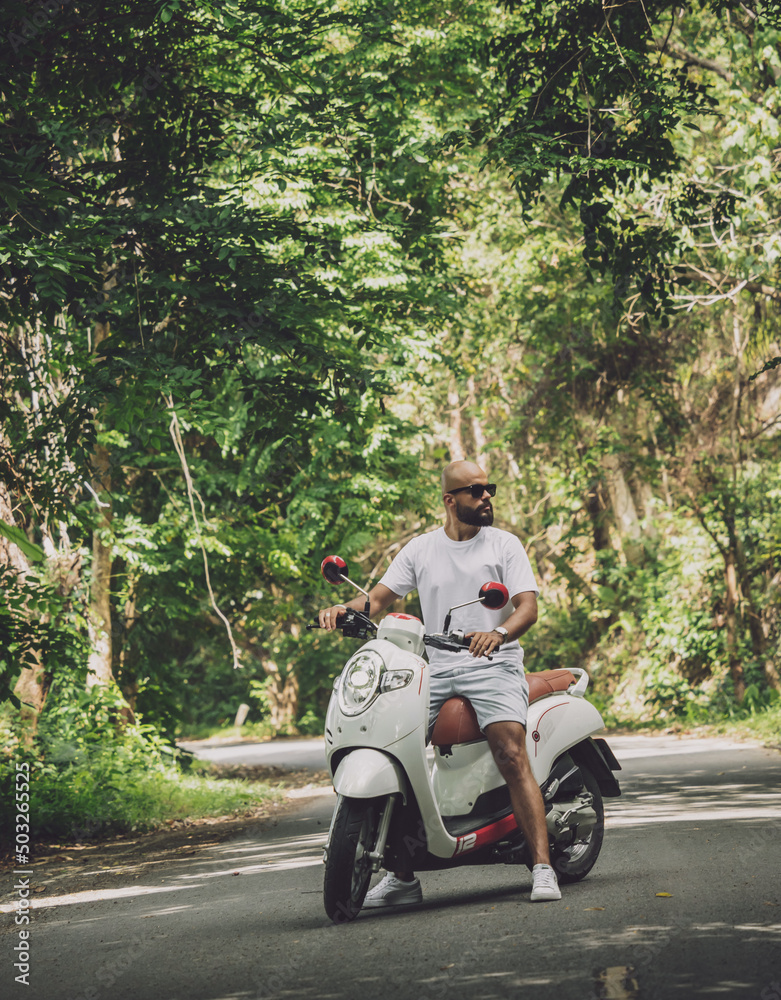 Stylish young man and his motorbike on the road in the jungle Stylish young man and his motorbike on the road in the jungle