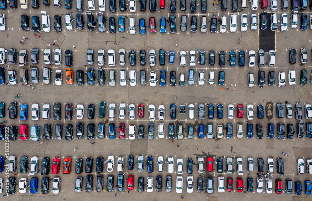 Many cars are located in a large parking lot near the shopping center (market). Aerial view.