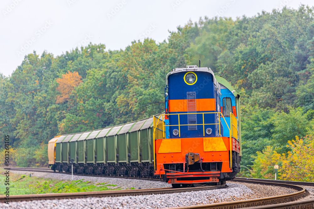 Obraz premium The locomotive pulls wagons loaded with grain from the elevator to the railway station. Summer evening lighting. Close-up view.
