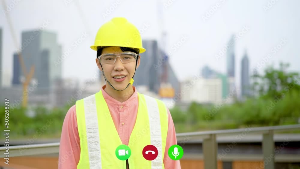 Asian engineer man having video call and waving a hand greetings to colleagues while looking at city landmark at background. contractor planning a project architecture building. Asian engineer man having video call and waving a hand greetings to colleagues while looking at city landmark at background. contractor planning a project architecture building.