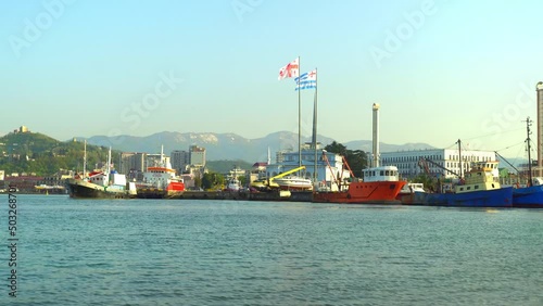 BATUMI, GEORGIA - APRIL 28, 2022: Boats are in bay while mooring boats in sea off coast. In background are mountains, clouds. Beautiful landscape, harbor. Flag of Georgia is raised. photo