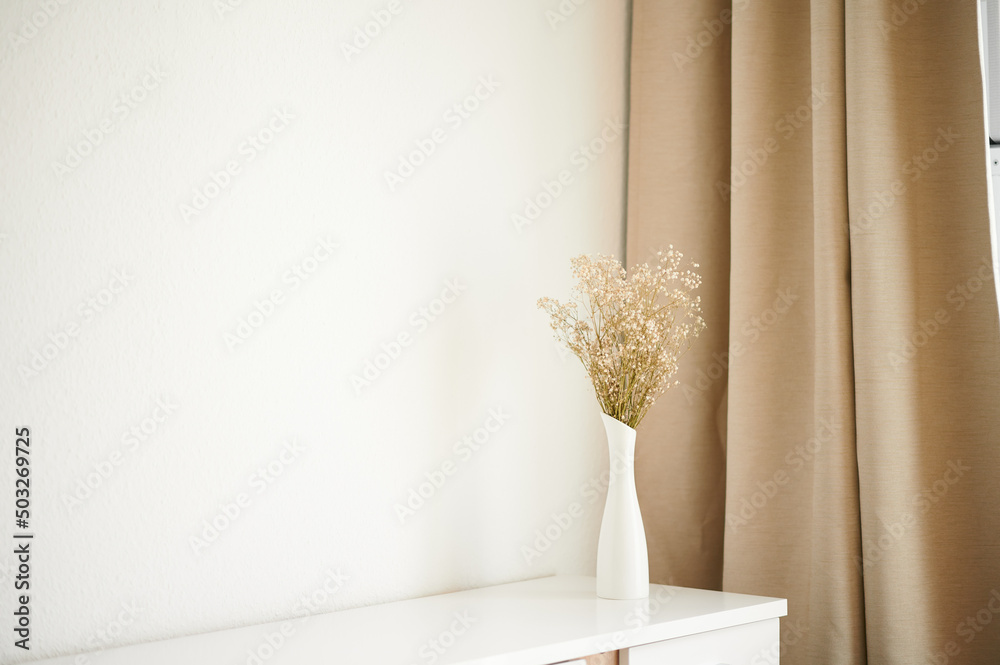 Yellow dried flowers stand in a minimalist interior. Golden curtain. Dried flowers in a white vase.