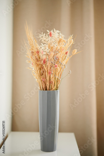 Dried flowers of wheat stand in a gray vase on a golden background. Minimalistic interior in pastel colors.