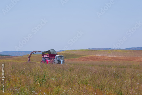 Agriculture, red combine tractor drives through the field, harvests sage