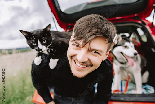 Husband cat on shoulders and husky dog in the background in the car.