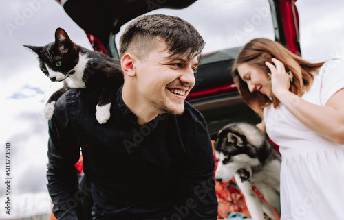 Husband cat on shoulders and husky dog in the background in the car.