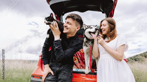 Pregnant woman with husky and cat on man's shoulders near car in car on nature background. Travel concept with pets.