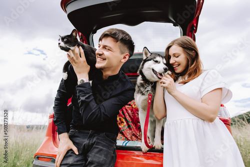 Pregnant woman with husky and cat on man's shoulders near car in car on nature background. Travel concept with pets.