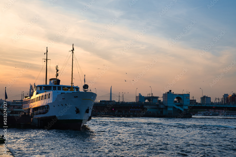 Evening scene on the Bosporus in Istanbul, Turkey, with a big ship in the foreground and the Galata Brigde in the background during sunset. 