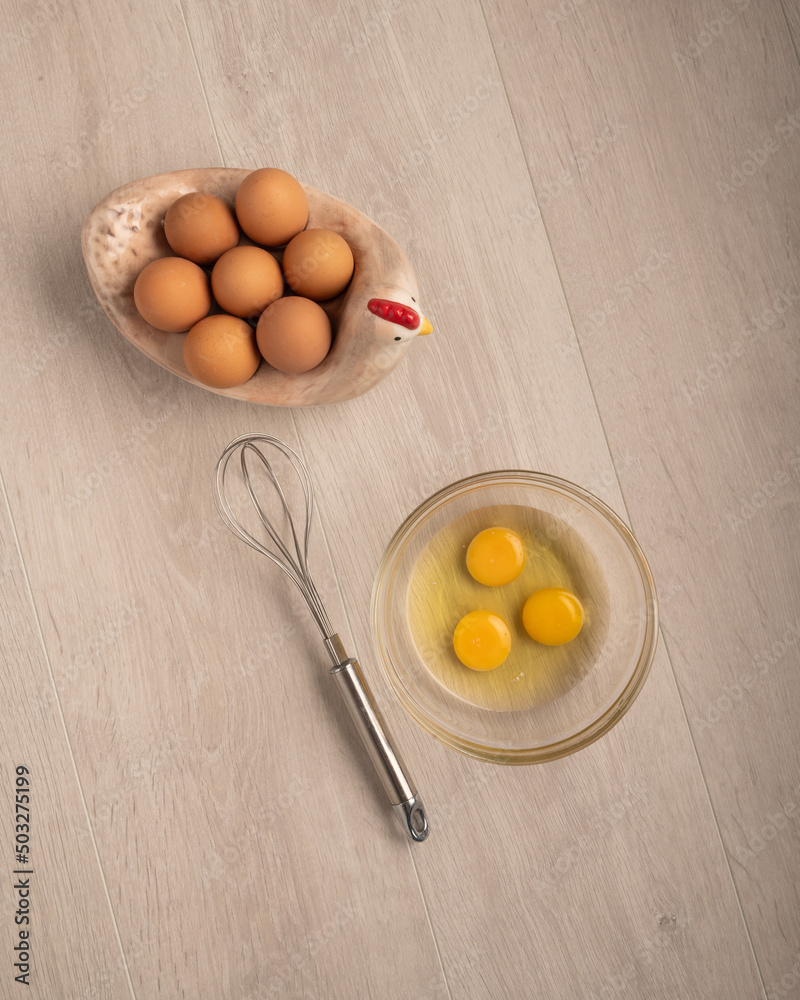 Organic eggs in a chicken shaped bowl and a whisk on a light wood background Organic eggs in a chicken shaped bowl and a whisk on a light wood background