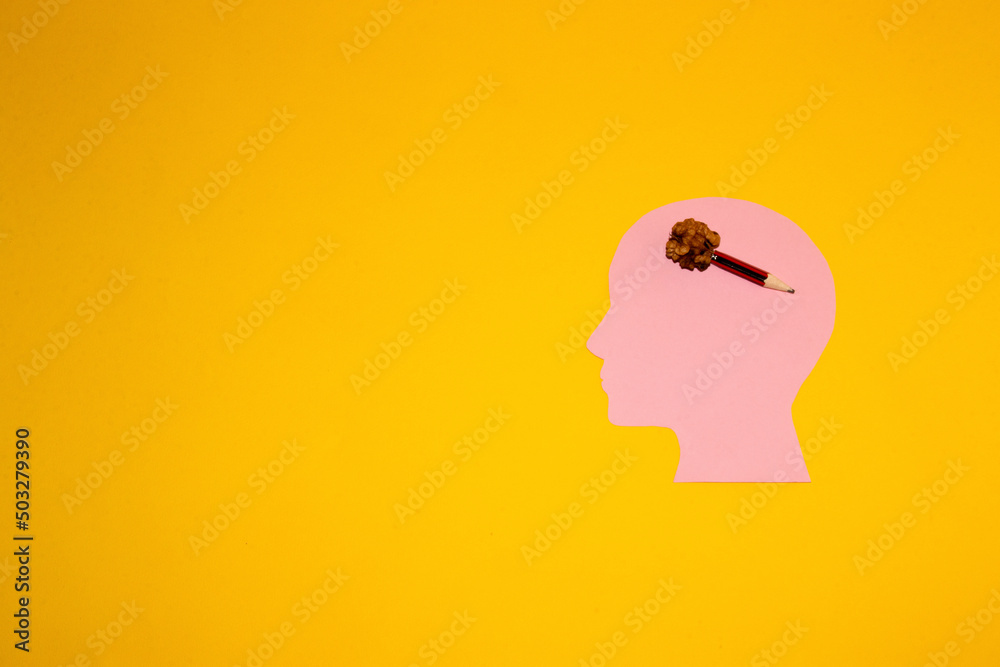 pink paper head with walnut and pencil on a yellow background, creative creation of ideas in the head