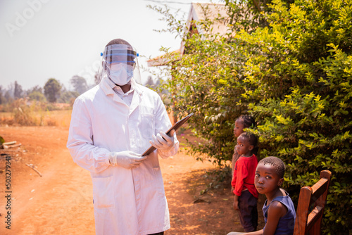 an African pediatrician visits child patients ready to be examined  wearing a face mask  a face shield and goggles to protect themselves during the pandemic