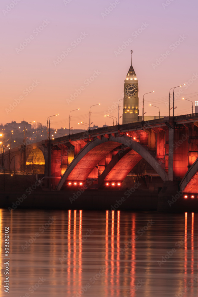 Obraz premium Krasnoyarsk Clock Tower is located in the center of Krasnoyarsk city in Russia against the background of a communal bridge with a beautiful red backlight across the enisey river