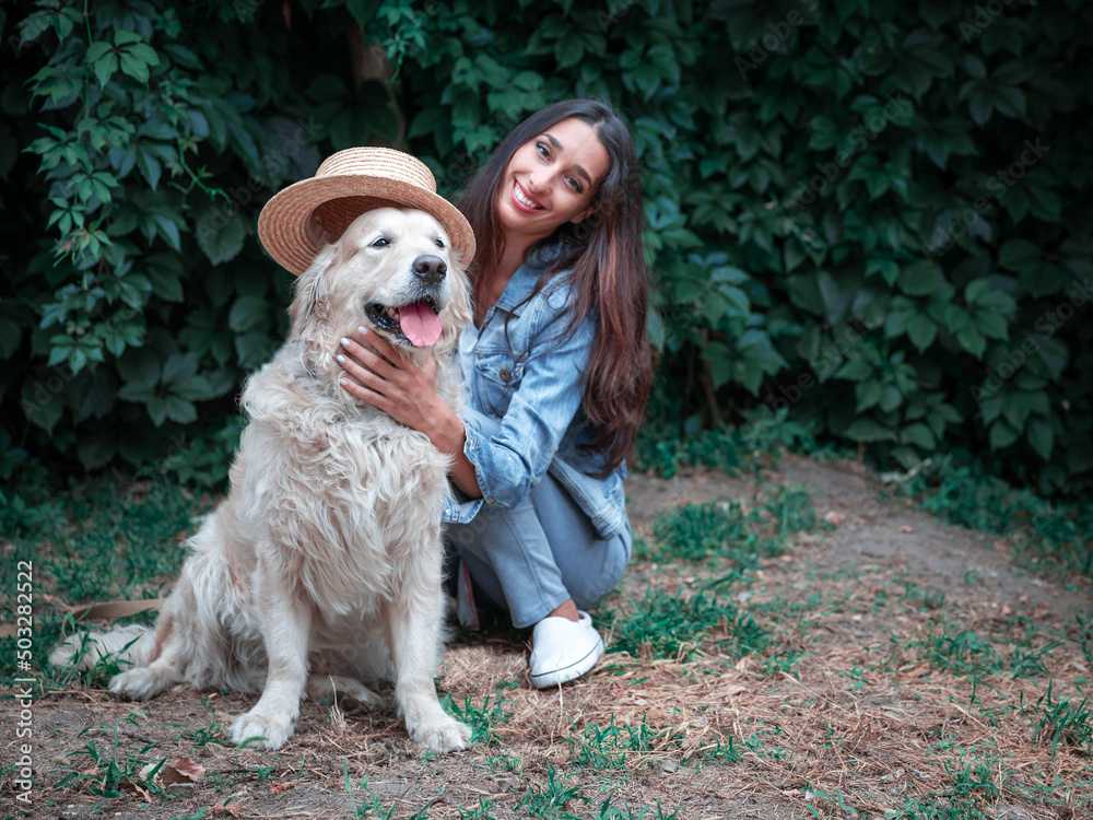 Portrait of yound happy woman playing with golden retriever labrador dog and straw hat