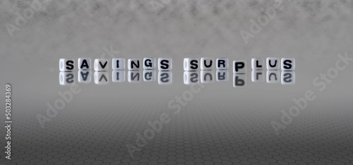 savings surplus word or concept represented by black and white letter cubes on a grey horizon background stretching to infinity