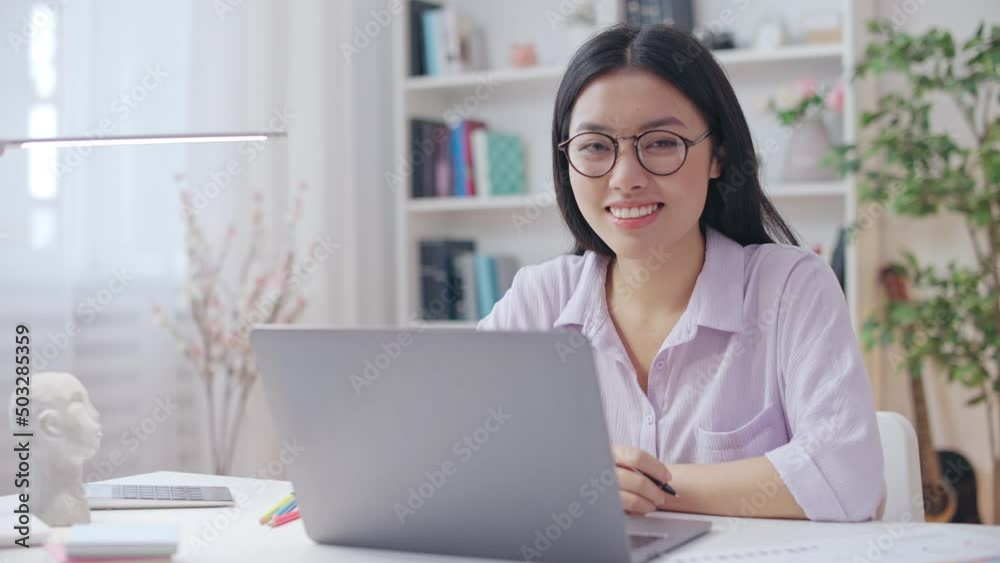 Successful Asian woman smiling, working on laptop in comfortable home office Successful Asian woman smiling, working on laptop in comfortable home office