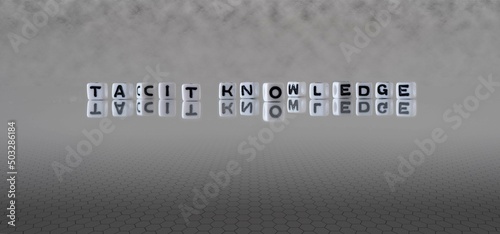 tacit knowledge word or concept represented by black and white letter cubes on a grey horizon background stretching to infinity