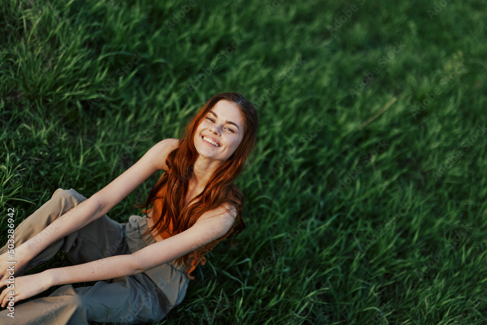 Happy woman smiling beautifully and looking up at the camera sitting on fresh green grass in the summer sunshine Happy woman smiling beautifully and looking up at the camera sitting on fresh green grass in the summer sunshine