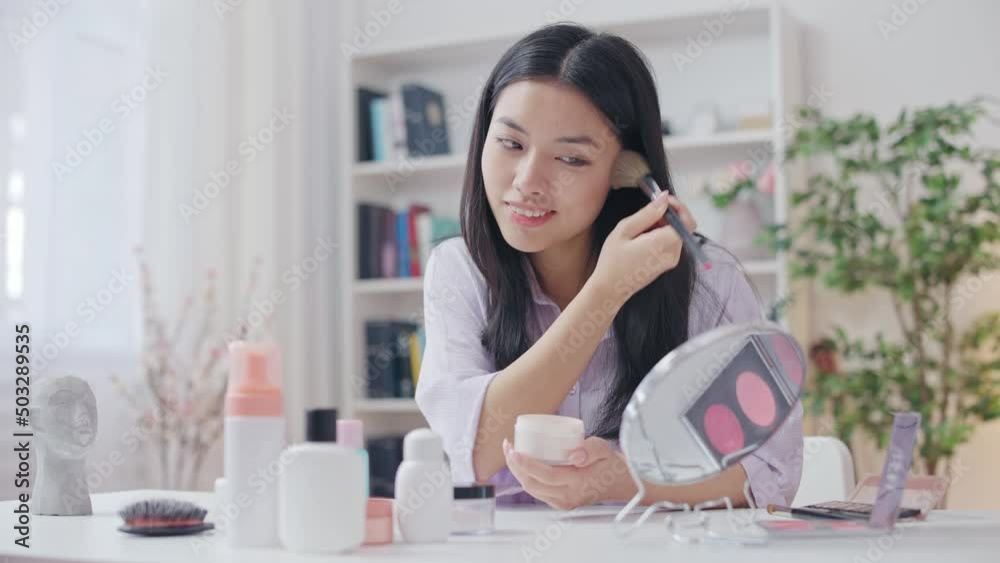 Smiling Asian woman applying make-up, enjoying reflection in mirror, beauty