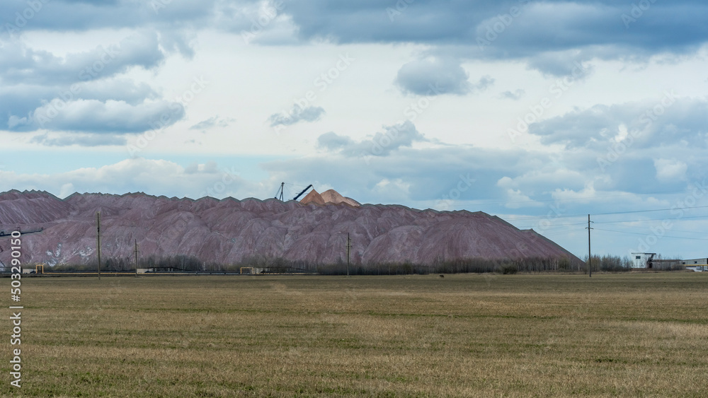 Mountains of empty ore when mining potassium on cloudy sky background. Transportation of an empty rock to a dump.