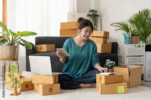 Asian woman entrepreneur using calculator with pencil in her hand, calculating financial expense at home office,online market packing box delivery,Startup successful small business owner, SME, concept © Natee Meepian